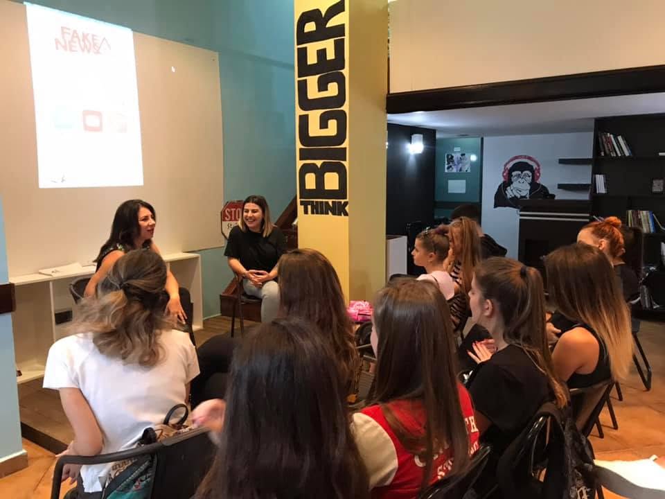 Pjesëmarrës duke dëgjuar dy folëse pranë një kolone të verdhë me shkrimin “Think Bigger”.