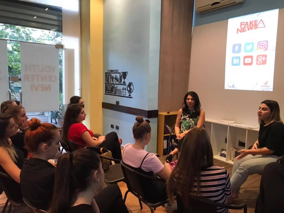 Bashkëbisedim në rreth: dy folëse përballë pjesëmarrësve, në ekran shfaqet tema “Fake News”.